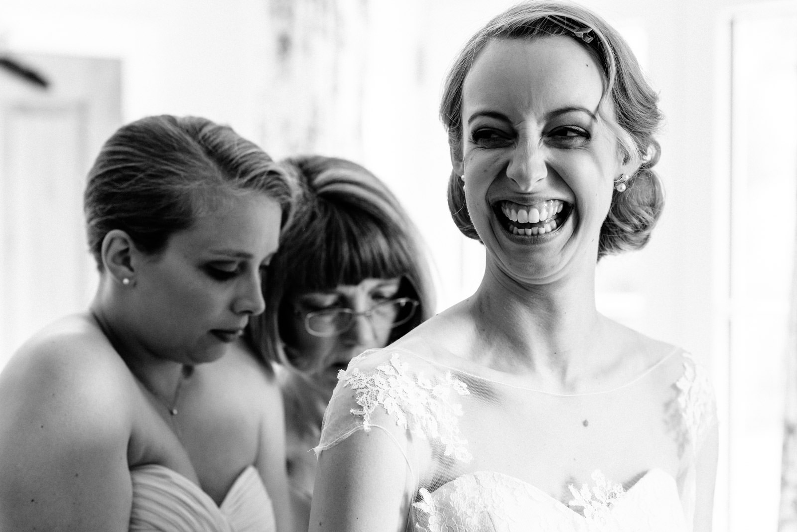 bride smiling while mum and bridesmaid help get her in dress