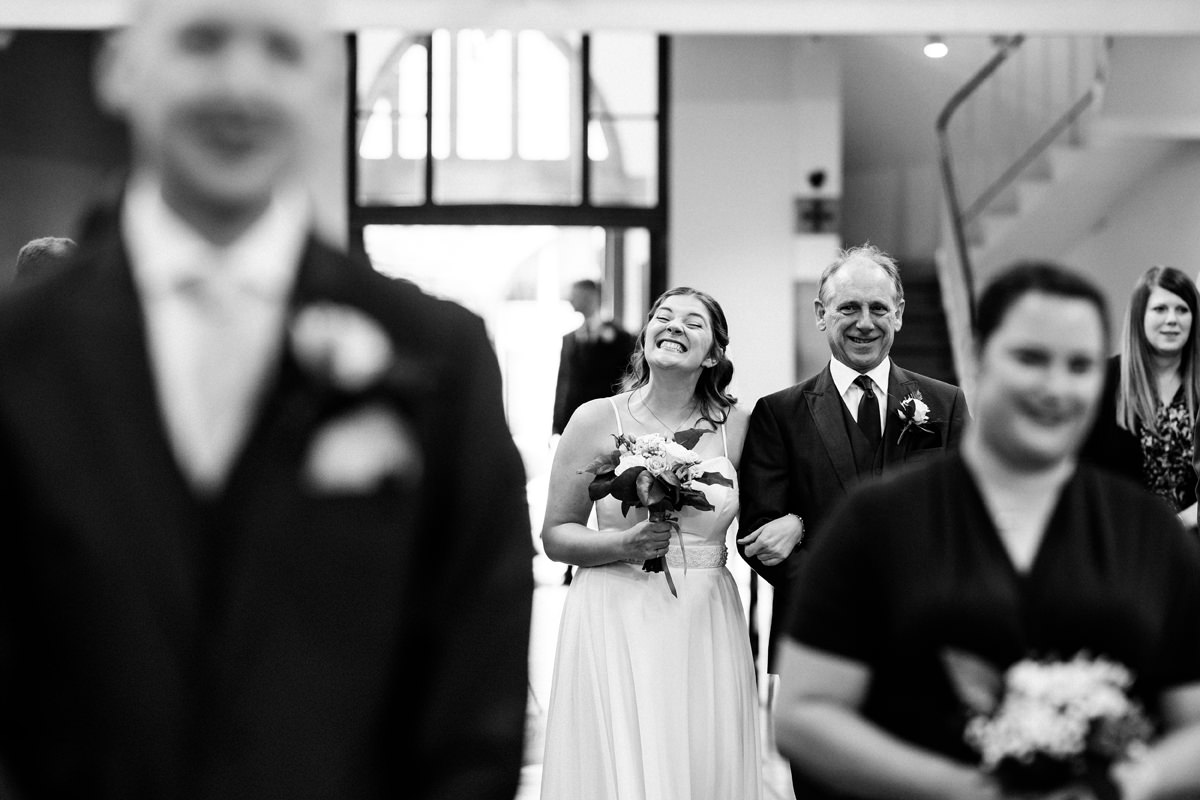 bride grinning as she walks down the aisle with her father