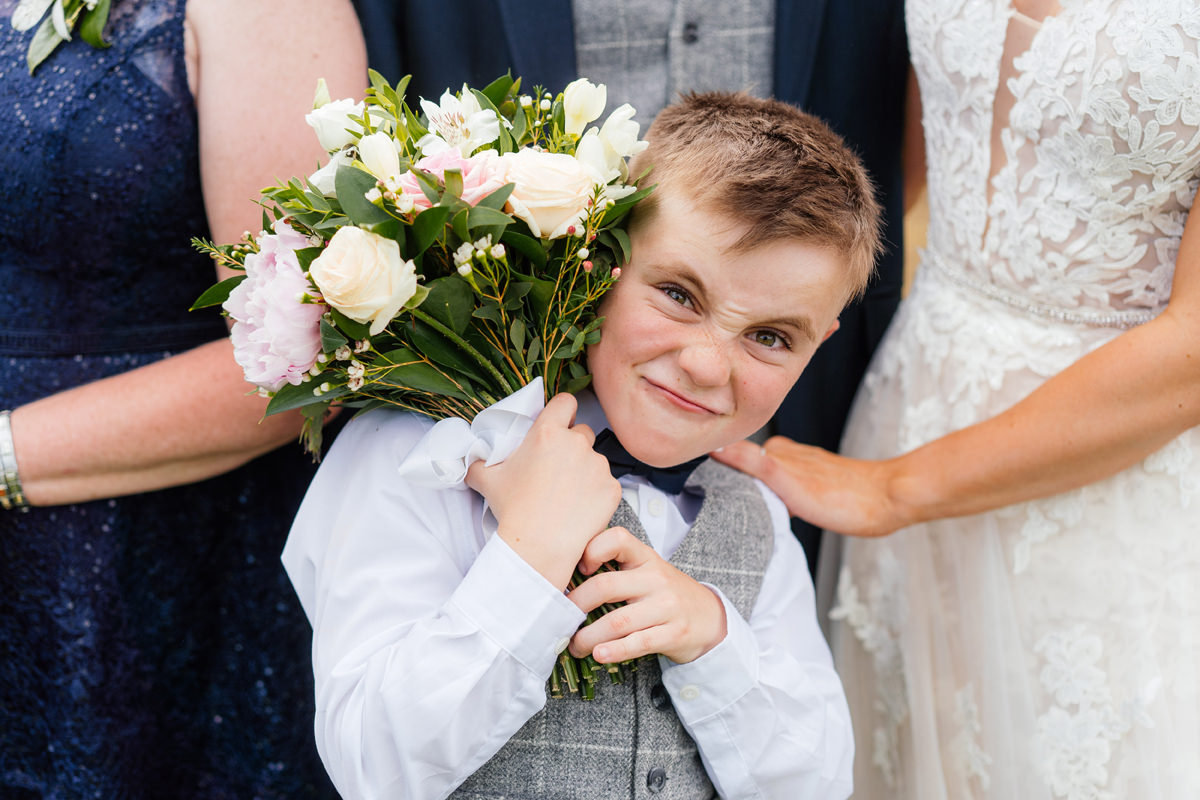 Page boy holding brides bouquet of flowers pulling a silly face