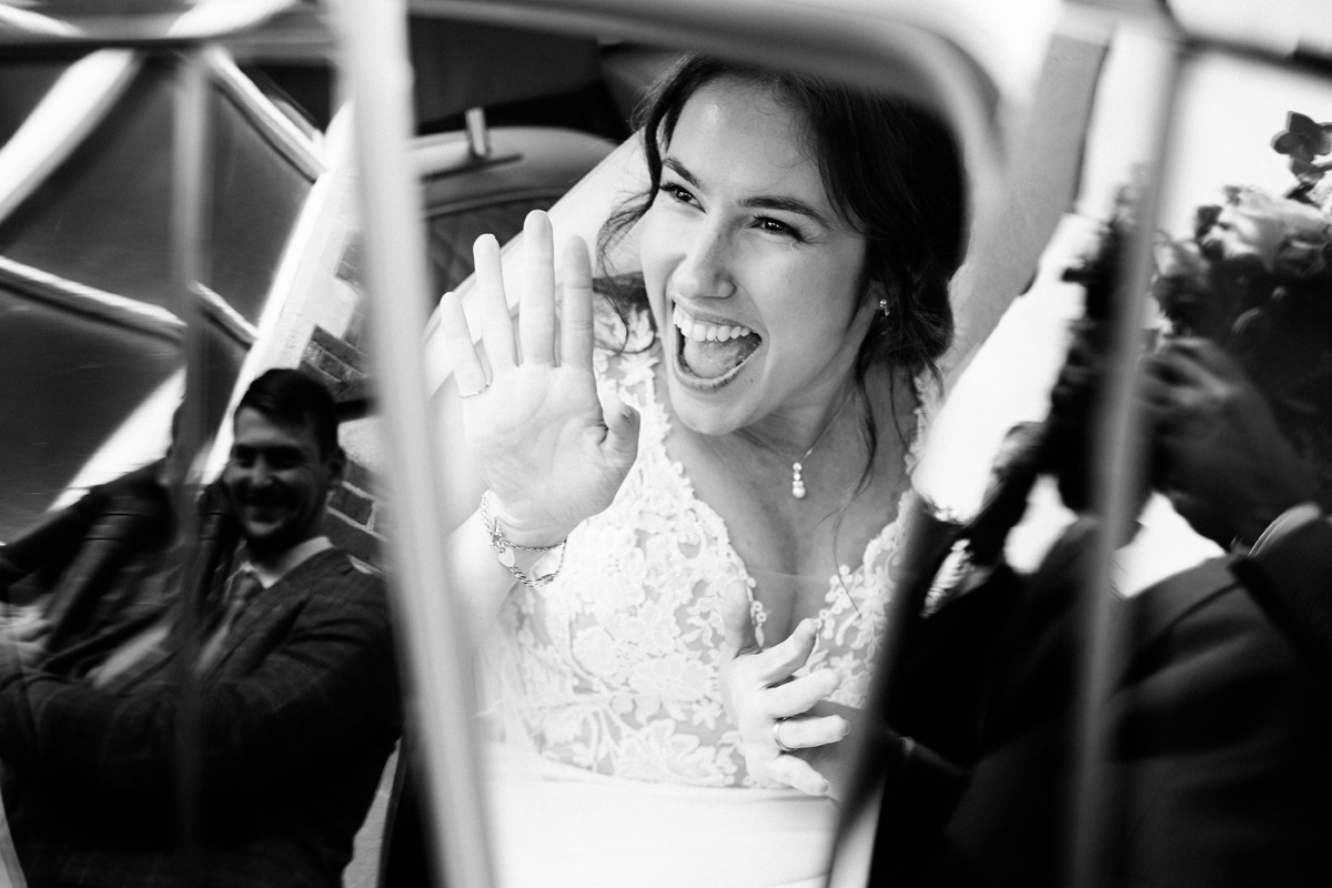 Bride waves goodbye from the car after the marriage ceremony