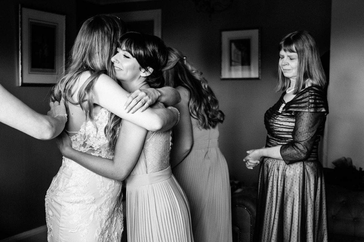 bride and the bridesmaids hug while the mother of the bride looks on