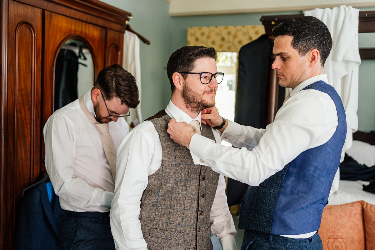 groomsman helps the groom with his tie