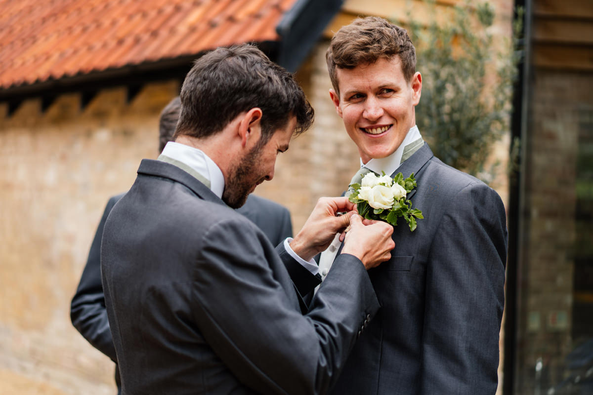 Groom having his button hole put on his jacket by a groomsman