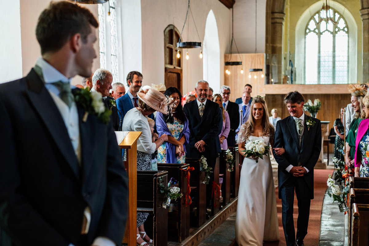 bride makes her entrance in the church with her father walking her down the aisle