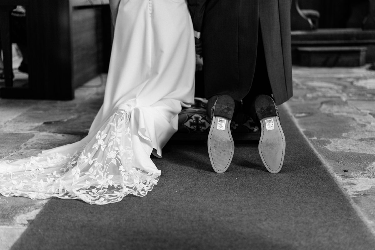 bride and groom kneeling for a blessing in the church the groom has forgotten to take his labels off the his shoes