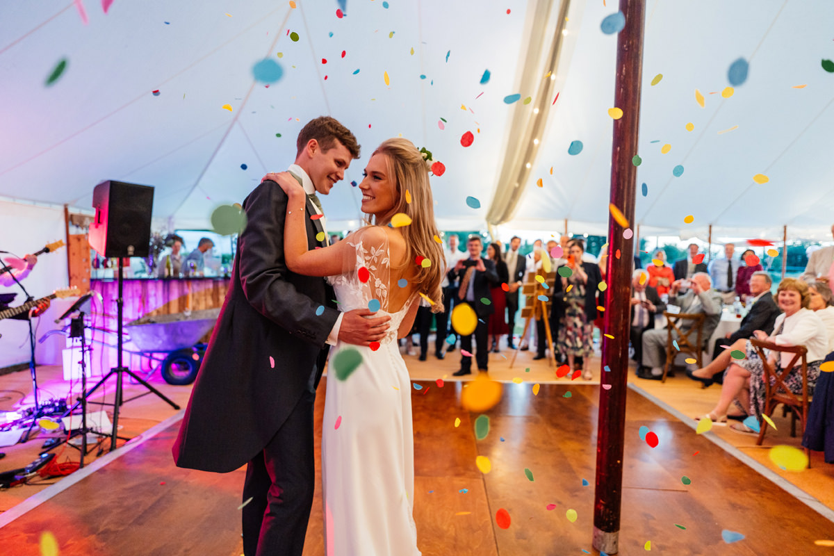 bride and groom take their first dance in the marquee with big confetti showering them