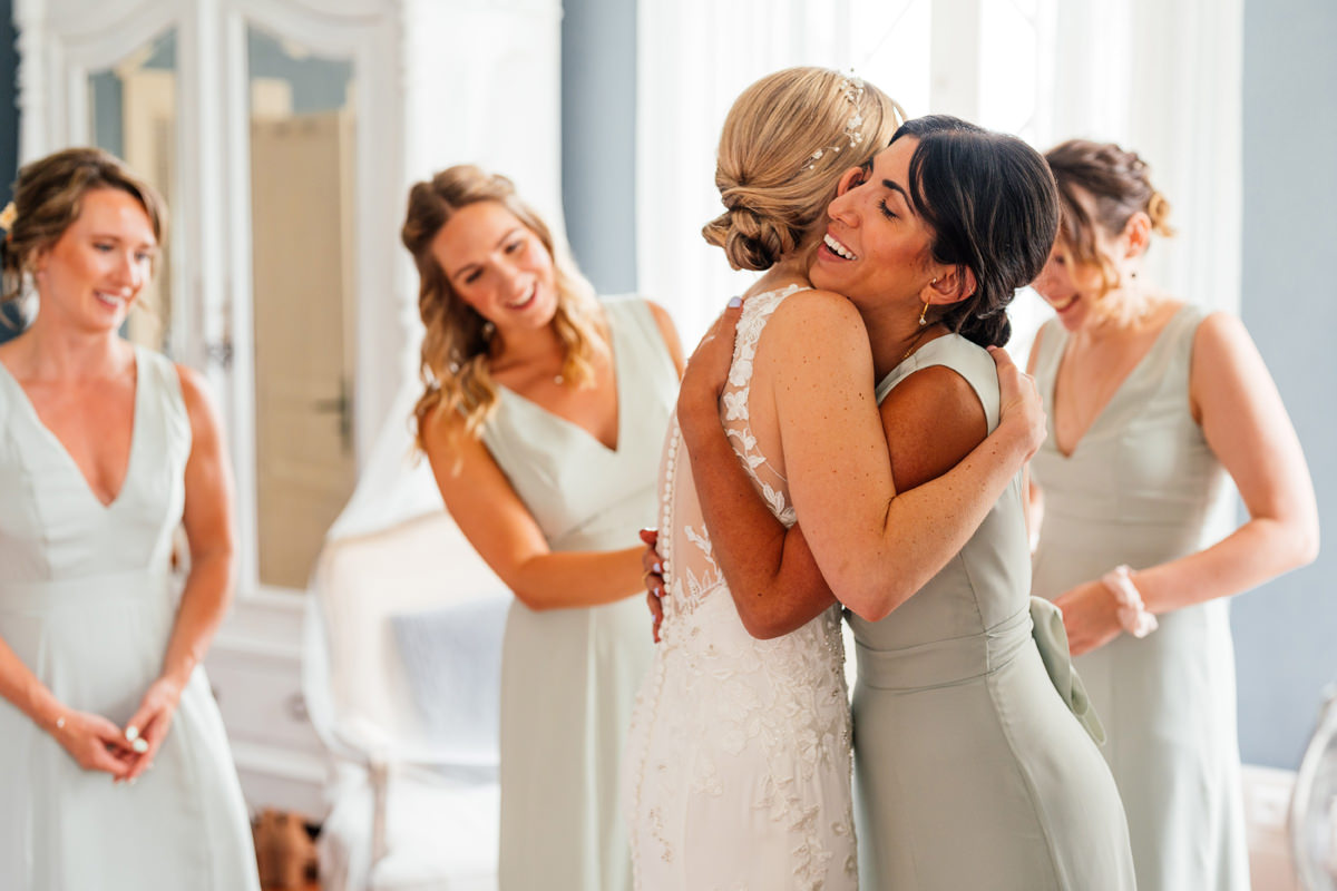Bride embraced by her bridesmaid after seeing her in the wedding dress for the first time.