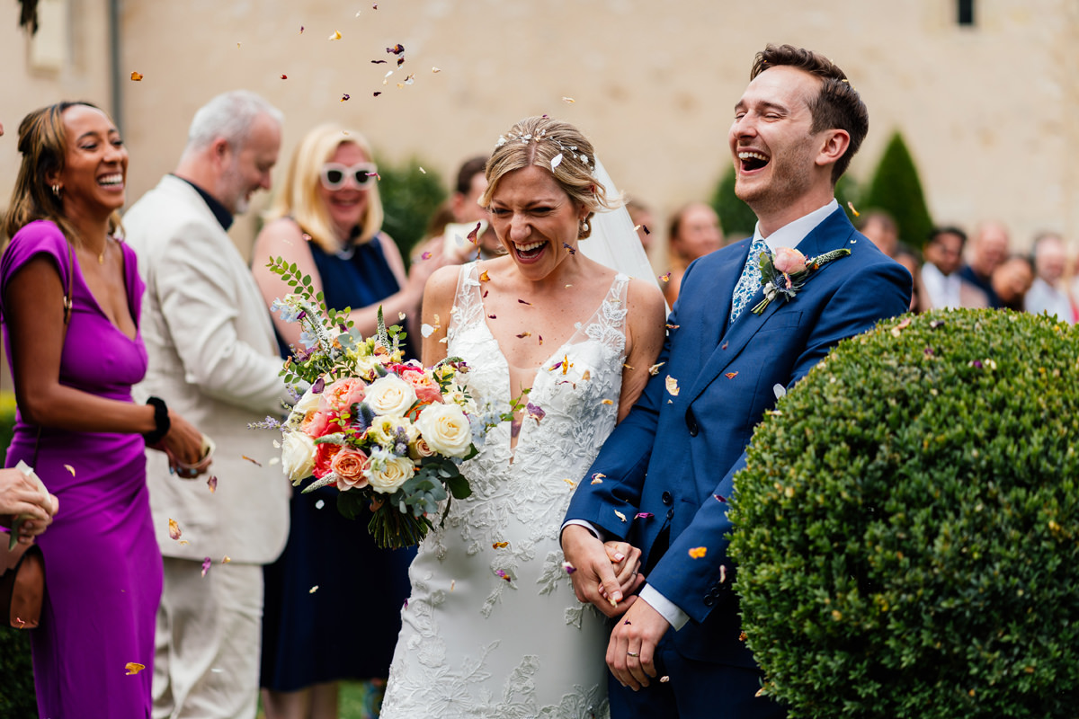 Bride and groom laughing and smiling as they walk through friends and family showering them with confetti